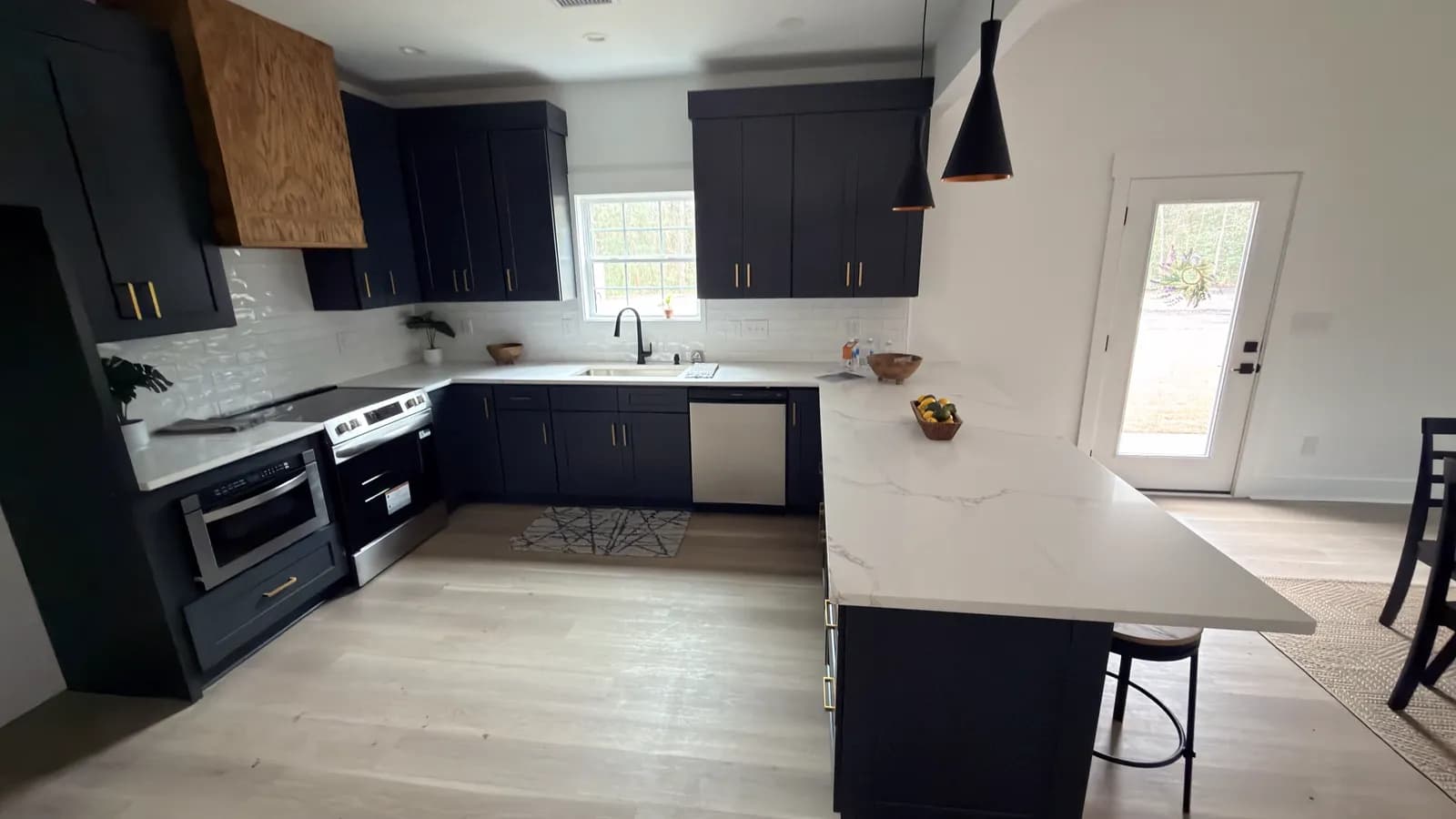 Navy Shaker kitchen with a natural white oak range hood and quartz peninsula, built by TS Cabinets